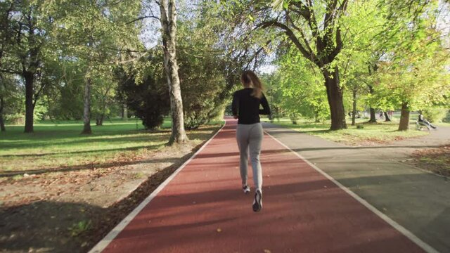 Fitness girl running on an all weather synthetic track surface over a wooden bridge in the park. Full body shot