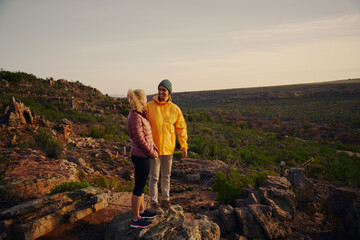 Handsome man looking at beautiful girl smiling after hiking and reaching mountain cliff edge