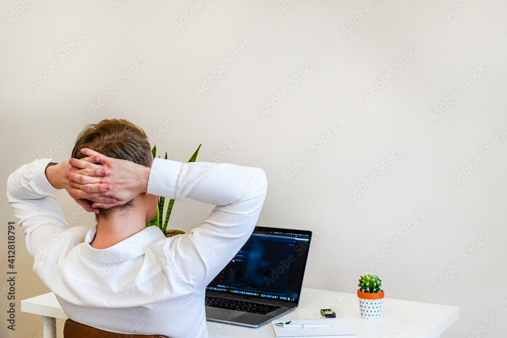 Canvas Prints a male programmer works with a laptop. the man is resting, sitting with hands behind head