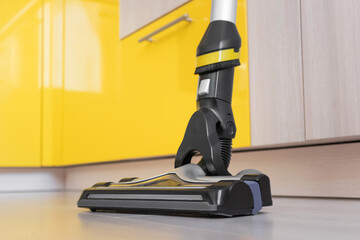 Upright vacuum cleaner brush on the laminate floor close-up. In the background are lockers. Beige, gray and yellow shades. House cleaning concept.