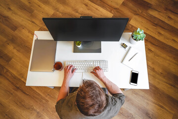 A male programmer works in front of a laptop screen in a bright office or remotely from home. Workplace