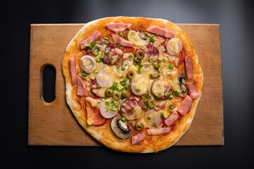 Pizza with mushrooms and sausage. fresh pizza on wooden board on black.