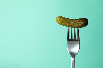 Fork with pickled cucumber on mint background