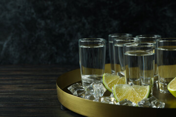 Tray with shots, lime slices and ice cubes on wooden background