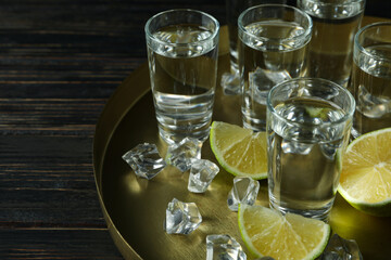 Tray with shots, lime slices and ice cubes on wooden background