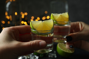 Female hands cheers with shots of vodka against blurred lights