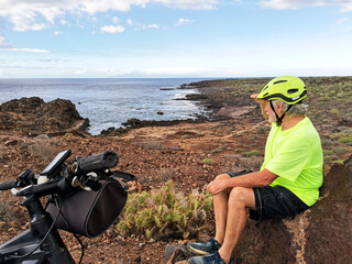 Senior man with bicycle and protective helmet enjoying the outdoors and the seascape. Healthy life of a carefree retiree