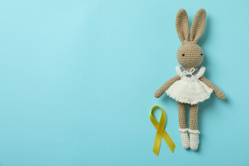 Toy bunny and childhood cancer awareness ribbon on blue background