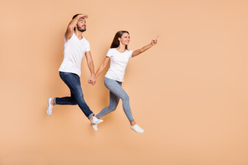 Fototapeta na wymiar Full length photo of young couple happy smile jump go girl point finger empty space guy look ahead isolated over beige color background