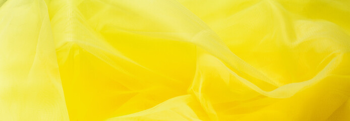 The colors of 2021 are yellow. abstract yellow tulle fabric background. wavy folds, waves of...