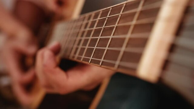 Family gatherings. Dad plays guitar holding one hand on fingerboard and other on body and his wife and little daughter also run their fingers along strings of classic acoustic six-string guitar