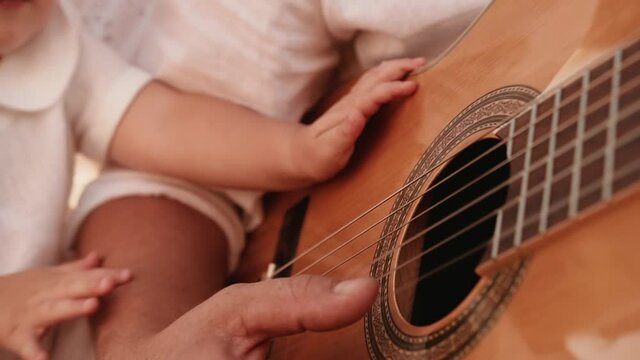 Family gatherings. Dad plays the guitar and the little daughter sits in mom's arms and also wants to rumble and beats a tiny handle on the strings of a classic acoustic six-string guitar