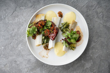 meat with bone with sauce with tomatoes and herbs on a white flat plate in the author's presentation from the chef
