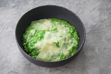 risotto with basil and parmesan cheese in a black plate on a gray background
