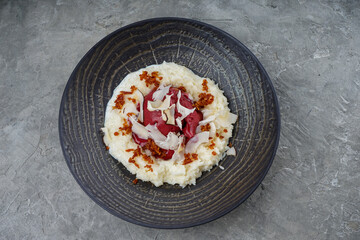 porridge with cheese mousse in a black plate on a gray background
