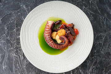 large octopus tentacles in a plate with grilled vegetables on a dark textured background
