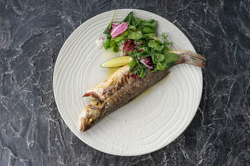whole grilled fish on a plate with salad on a dark background

