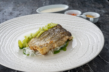 fillet of riba with skin on a pillow of salad in a white plate on a dark background

