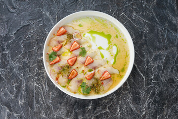 squid carpaccio decorated with strawberries in a white plate on a dark background
