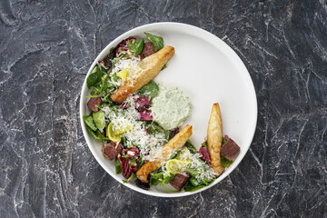 salad with meat cheese and fresh vegetables with sauce on a white on a dark textured background top view
