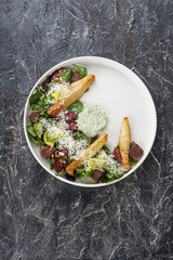 salad with meat cheese and fresh vegetables with sauce on a white on a dark textured background top view vertical
