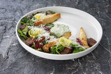 salad with meat cheese and fresh vegetables with sauce on a white on a dark textured background
