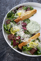 salad with meat cheese and fresh vegetables with sauce on white on a dark textured background close-up vertically
