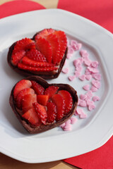 Fototapeta na wymiar Two mini heart shaped chocolate tarts with fresh strawberries on a plate on a wooden table