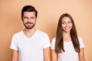 Portrait of two young satisfied persons look at each other smile isolated on beige color background