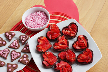 Valentine’s day dessert background. Mini heart shaped chocolate tarts with fresh strawberries and glazed ccokies with sprinkles on a wooden table