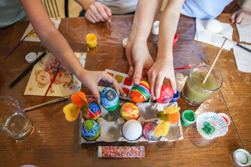  family decorates eggs for Easter. In the frame only outstretched hands holding eggs over a crafting stand on the table