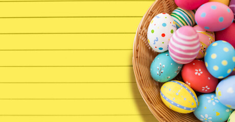 easter, holidays and tradition concept - close up of colored eggs in basket over yellow wooden boards background