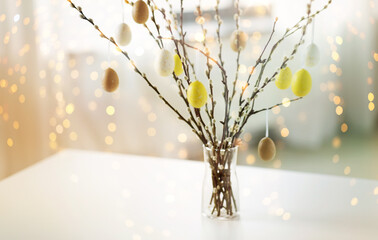 holidays and object concept - pussy willow branches decorated by easter eggs in vase on table over bokeh lighs