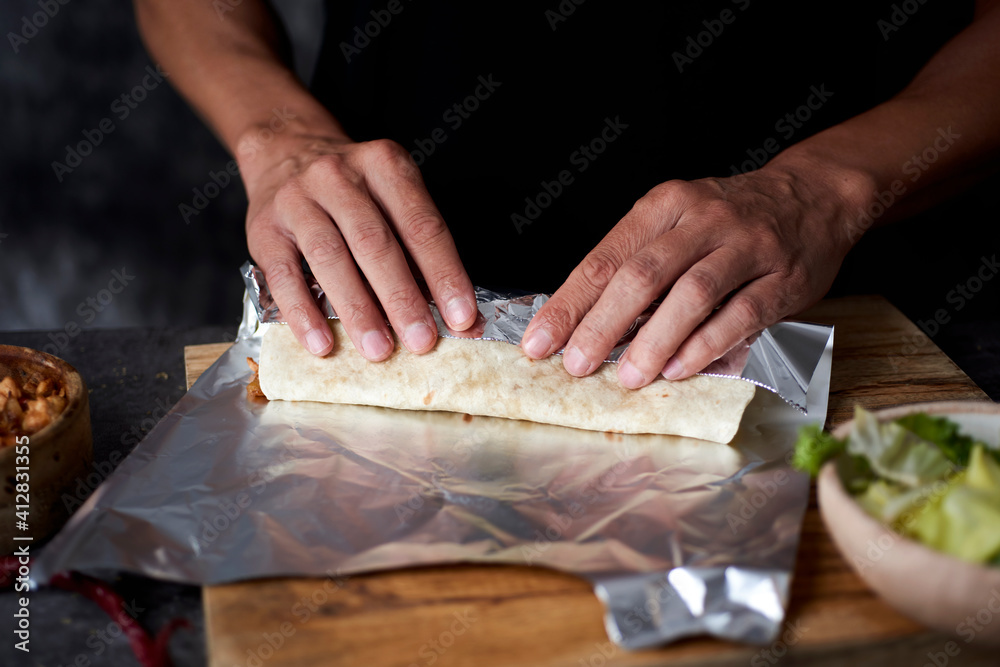 Poster man wraps a durum or a burrito in aluminum foil