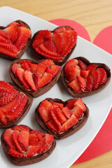 Valentine’s day dessert background. Mini heart shaped chocolate tarts with fresh strawberries on a plate on a wooden table