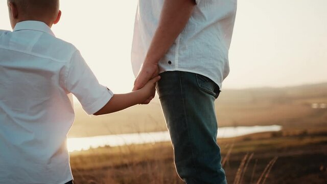 Child boy and adult dad equally dressed stand at gold field at sunset and holding hands. Son looks away and shows something father. Happy family day parent spend with lovely kid. Raising little man
