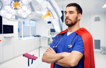 healthcare, surgery and medicine concept - doctor or male nurse in blue uniform and red superhero cape with stethoscope over hospital background © Syda Productions
