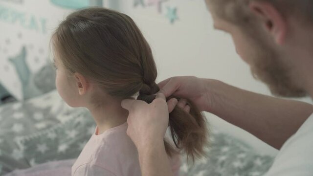 Father's day. Dad making a ponytail and combing his little daughter's hair at home.