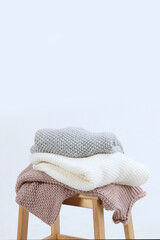Knitted woolen clothes lie on a wooden chair. Clothes made of natural wool for the cold season. Sweaters with chunky knits. Light background. No people. Copy space.