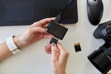 technology, post production and vlog concept - hands with sd memory card reader, digital camera and laptop computer working at office