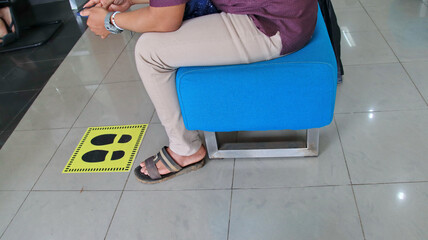 people waiting in line for a service and sitting on chairs with social distancing symbols