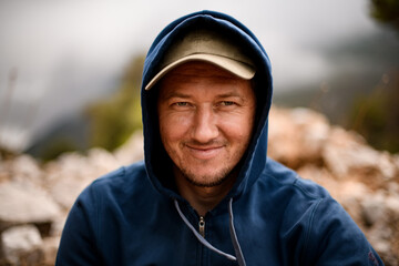 portrait of smiling man in cap and blue sweater with hood