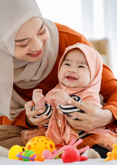 Beautiful Asian Muslim mather playing with her infant daughter baby in bed room with love and care....