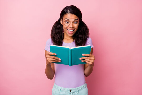 Portrait of charming cheerful amazed girl reading interesting novel isolated over pink pastel color background