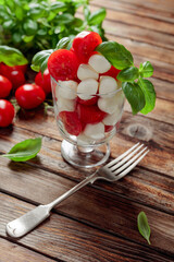 Caprese salad with tomato, mini mozzarella and basil on a old wooden table.