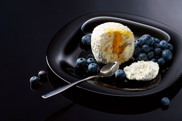 Cottage cheese with honey and blueberry on a black plate.