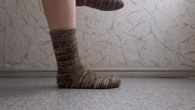 The girl takes off her woolen socks and shows her bare legs in close-up. Monochrome 4K video.