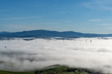 view of rolling hills landscape in Andalusia with many wind turbines above the fog in the valleys and blue sky above
