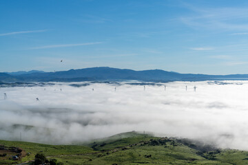 view of rolling hills landscape in Andalusia with many wind turbines above the fog in the valleys and blue sky above