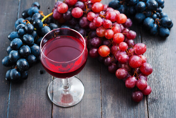 glass of red wine and grapes on black wooden table background